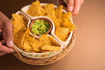 Hands taking some fried nachos in a pot with some fresh guacamole on a green surface 