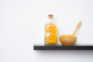Wooden spoon, bowl and bottle filled with yellow bath sea salt on the black shelf. Beauty treatment for spa and wellness. Skincare natural cosmetic concept for body care.