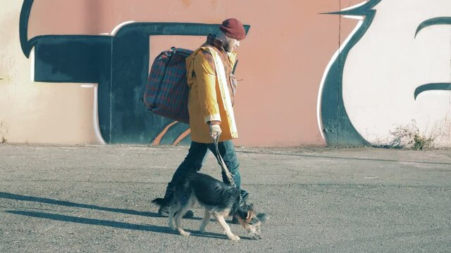 A homeless man is leading a dog along the city street