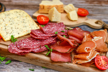 Italian  dried thinly sliced   artisan  pork salami Milano , parmesan cheese, tomatoes   and fresh basil on wooden background .Rustic  home made italian snack.