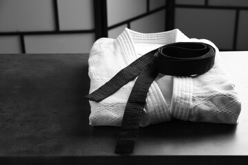 Martial arts uniform with black belt on grey stone table indoors - obrazy, fototapety, plakaty