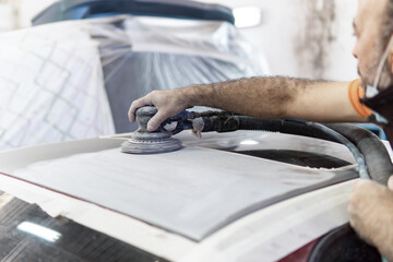 Auto mechanic sanding a part of a car in a garage. Preparing for painting the car in a workshop. Blurry movement