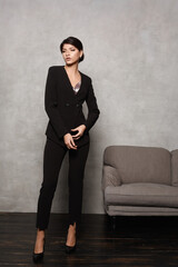 Charming young businesswoman wearing black office stylish suit posing in a minimalist interior