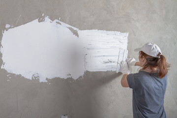A female construction worker puts a concrete wall in the house with a spatula with white putty