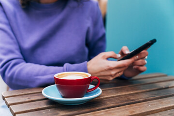 Crop woman using smartphone and drinking coffee
