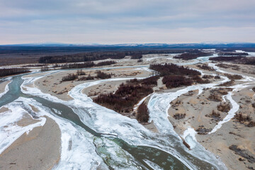 Aerial view of the freezing river. Top view of the winding stream beds. Icy river banks and islands with floodplain forest. Cold weather. Northern nature. Ola River, Magadan Region, Far East of Russia