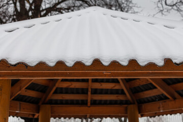 snow-covered roof of a wooden gazebo in a winter park