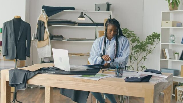 Successful Businessman-tailor, African-American Girl, Works with Sketches of Clothes, Using a Laptop. Creation of an Individual Costume in a Luxurious Atelier. Sewing Small Business, Fashion Industry.