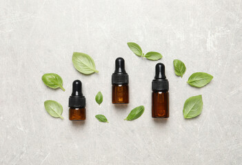 Bottles of essential basil oil and fresh leaves on light grey table, flat lay