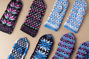 Set of different knitted mittens on beige background. Warm handmade mittens for winter. Pattern