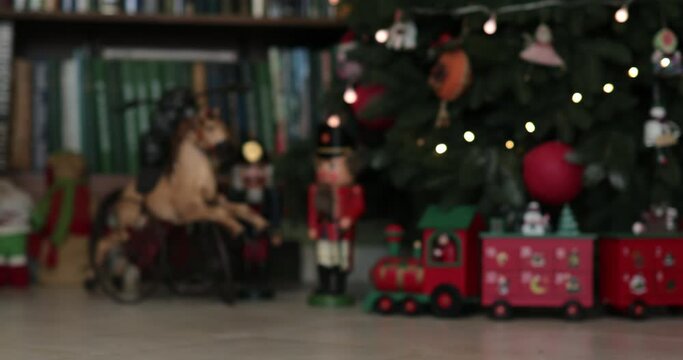 Advent calendar in shape of wooden train under faux Christmas tree decorated with retro Christmas ornaments. Antique nutcracker soldier toys and horse under faux fir tree. Moving from blur into focus