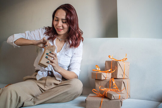 excited redhead woman looking at her gifts wrapped in recyclable paper, happy redhead woman opening her presen