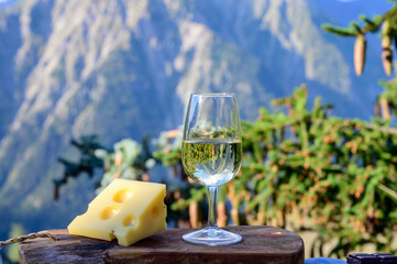 Glass of swiss or savoy dry white wine and yellow emmental cheese with Alpine mountains peaks on background