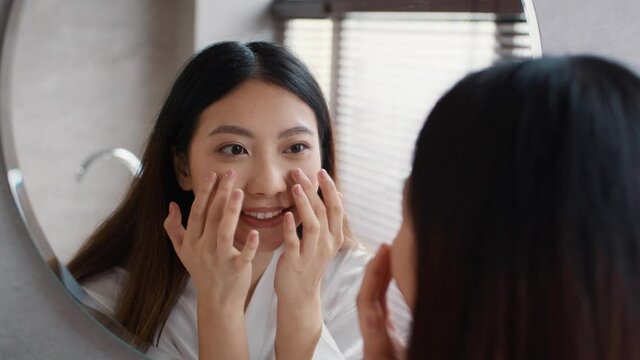 Face Massage. Young Beautiful Asian Woman Looking At Mirror And Touching Skin