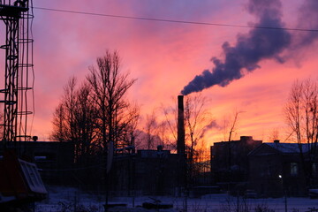 Bright colorful sunset over the city, smoky pipe, metal construction and tree