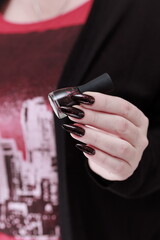 Female hands with long nails and black and red manicure holding a bottle of nail polish