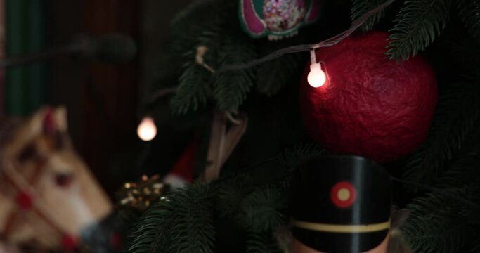 Soft focus to faux Christmas tree decorated with retro Christmas ornaments and lamp garland. Antique nutcracker toy and horse statuette closeup. Rack focus holiday background