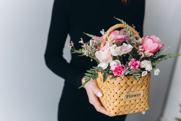 Bouquet of fresh flowers in basket in woman's hands