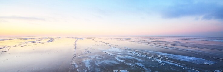 Snow-covered shore of the frozen lake at sunset. Stunning pink cloudscape. Symmetry reflections on...