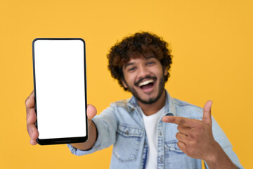 Happy excited young indian man showing smartphone pointing at big mockup white blank phone template...