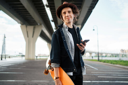 Playing on the phone. Portrait of Melinial in a hat a man riding a skateboard walking in the city alone.