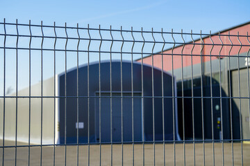 abstract blurred gray industrial building behind a grating wire industrial fence panels