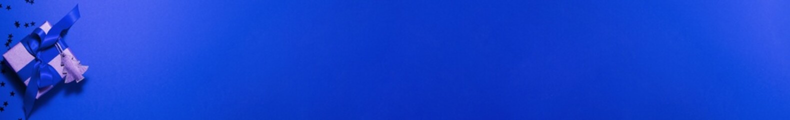 Banner of brown paper gift box with a blue satin ribbon bow with wooden tree and stars on top on blue Christmas holiday mother and father Valentines days birthday present flat lay concept copy space.