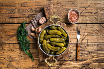 Pickled gherkins cucumbers in bowl with herbs. Wooden background. Top view