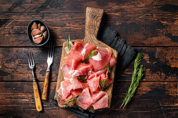 Slices of jamon serrano ham or prosciutto crudo parma on wooden board with rosemary. Wooden...