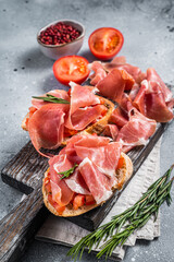 Spanish Tapas - Toast with tomatoes and cured Slices of jamon iberico ham on wooden board. Gray background. Top view