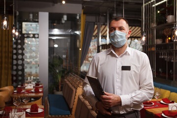 Fototapeta na wymiar Waiter wearing medical face mask, carrying menu, working at restaurant during quarantine