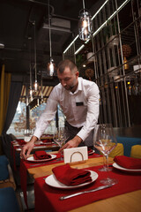 Vertical portrait of a male waiter preparing tables for customers at the restaurant