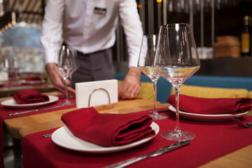 Selective focus on a wineglass and a plate on restaurant table, waiter working on background
