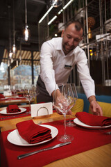 Vertical shot of a cheerful waiter enjoying preparing tables for restaurant guests