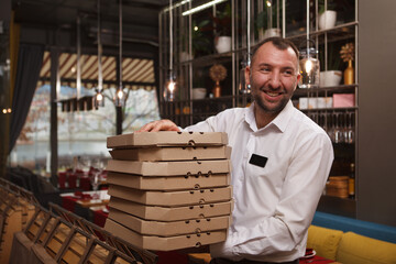 Cheerful waiter smiling, carrying many pizza boxes ready for delivery, copy space