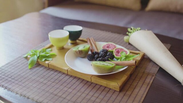 Delicious fruit dish on a plate with fragrant green tea on a wooden tray