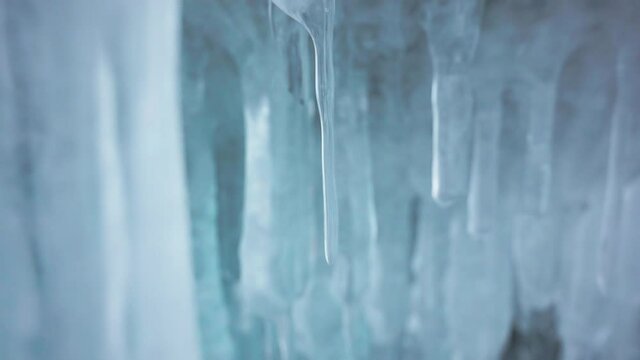 Smooth crystal clear white icicles hang inside ice cave. Frozen water formations