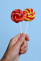 Woman holding bright tasty lollipops on light blue background, closeup