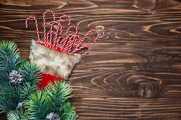 Christmas card with fir branches, santa hat and lollipop candies on wooden background.