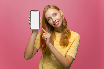 Cheerful young girl showing modern phone with blank mock-up screen. New entertaining or dating mobile app advertising