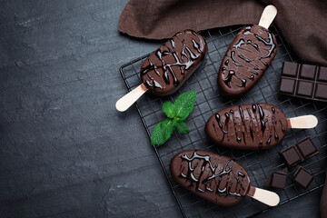 Delicious glazed ice cream bars, chocolate and mint on black table, flat lay. Space for text