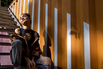 Latin woman (20) sitting on stairs with closed eyes, orange container background and natural light. Young people concept.