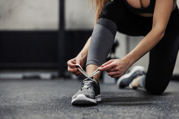 Tying shoelaces on sneakers before training. A girl in black and gray sportswear squats on the...