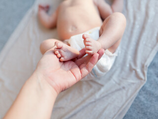 Mother holding her newborn baby's tiny feet in her hand. Shallow DOF and soft natural lighting.