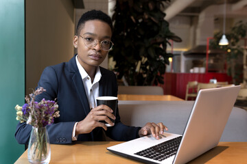 Serious and focused business woman working in a hotel restaurant, African American woman traveling...