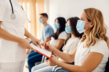 Obraz premium Health care and medical service. A woman signing up the form in the hospital hall while the nurse is holding it and pointing where to sign.