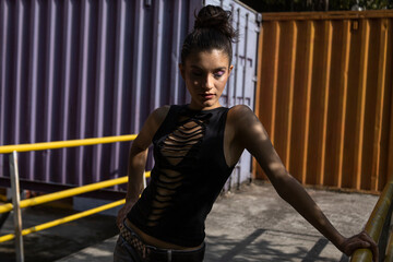latin woman (20) standing, medium shot with torn pants and handmade shirt, purple container background. Young people concept.
