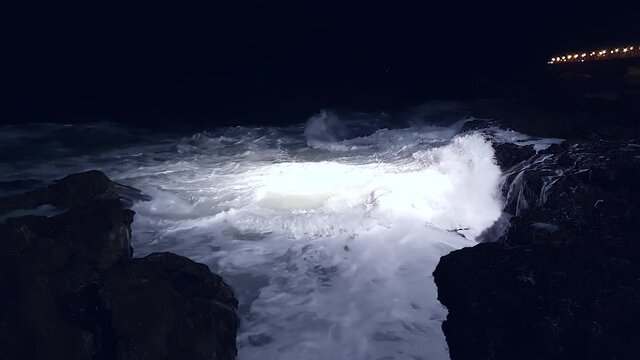 Sea waves splash and crash into rocks with much white foam. Night cinematic shot sea violently splashing over the rocky coast.