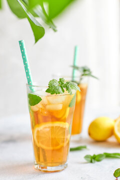 Iced iced tea in a glass with a straw, mint leaf and lemon slices inside. Cool drinks in the heat. Vertically photo