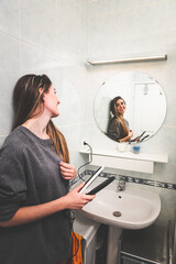 Young caucasian woman with a hair straightener in the bathroom.